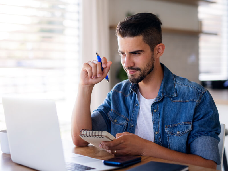 Man taking notes in his notebook while looking at the laptop