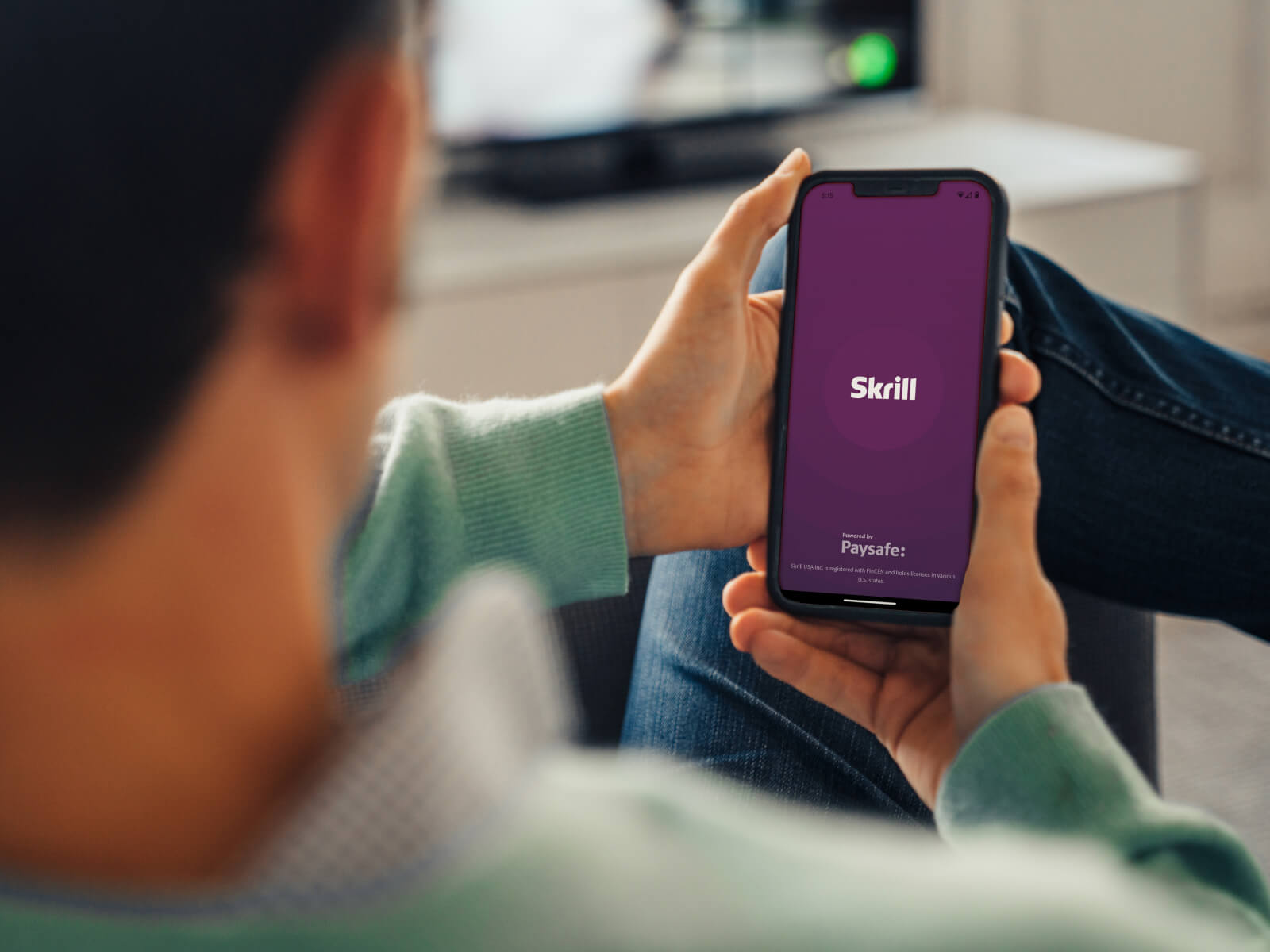 someone holding their phone open to the Skrill splash screen