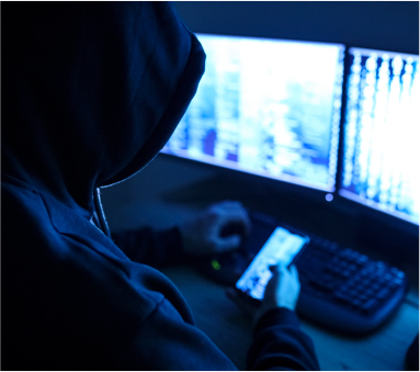man with a hoodie browsing his phone in front of monitors