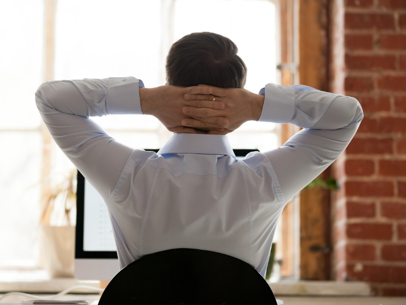 man with hands behind his neck staring at a desktop
