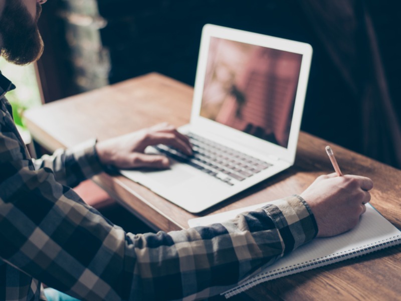 a man learning from a laptop and writing down notes