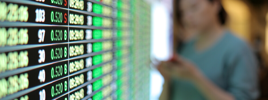 woman looking at a phone in front of foreign exchange monitor