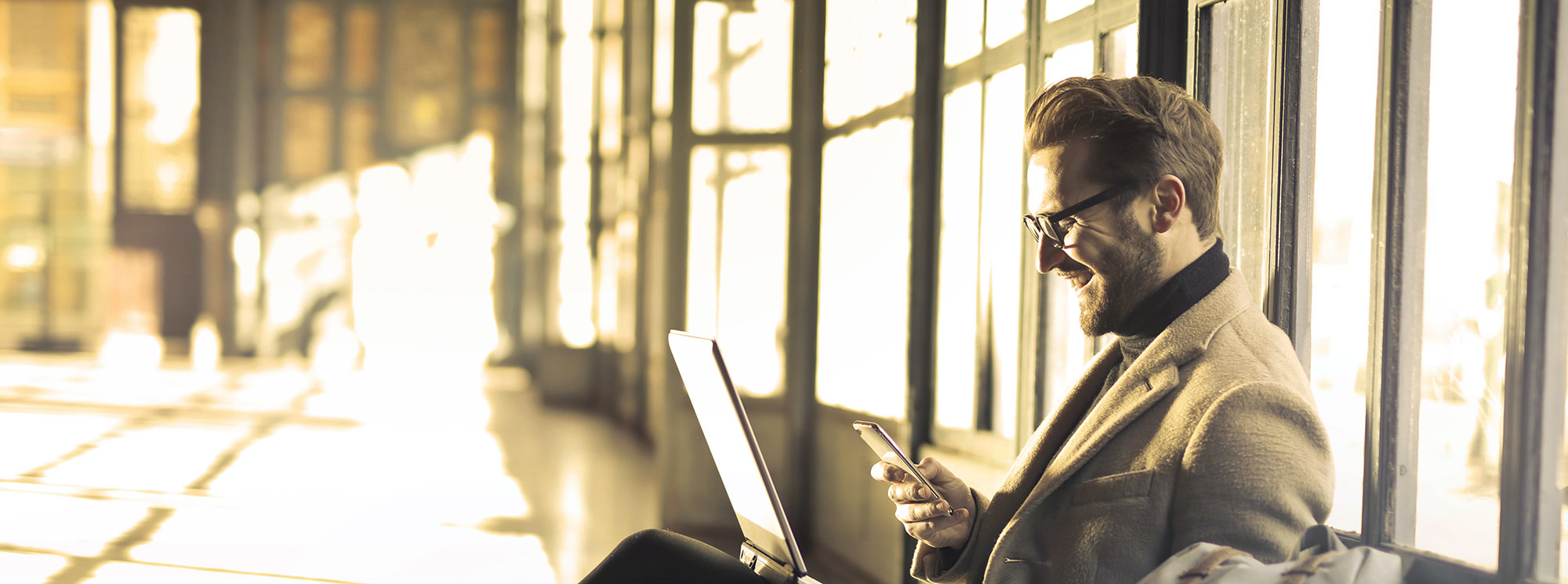smiling man working on his laptop in a large sunny space