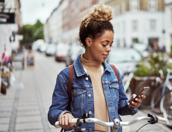 Young beautiful lady on a bike, stopped in the middle of the street and looking at her phone