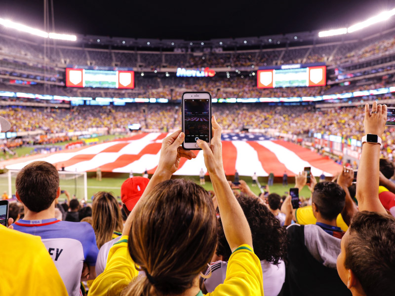 audience taking photo of the US flag carried by people on the stadium