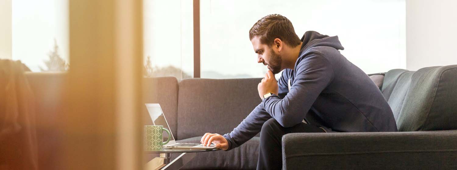 A man sitting on a couch browsing on a laptop