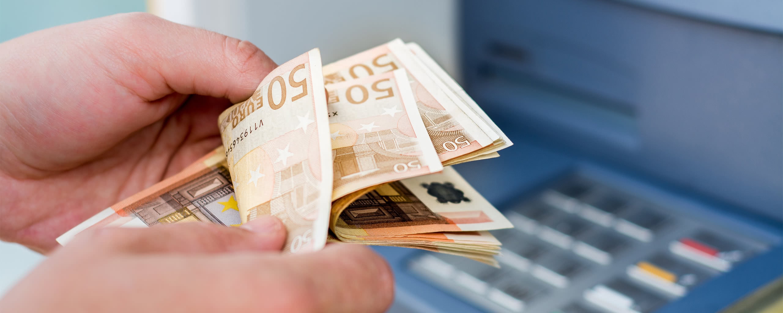 man counting money next to an ATM
